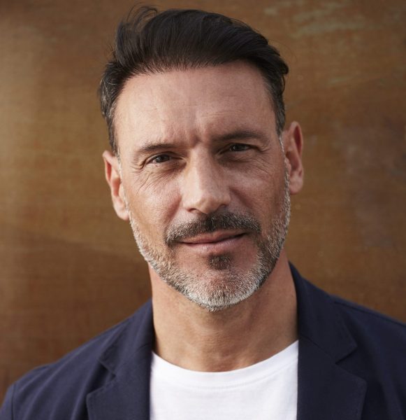 middle-aged-man-wearing-leaning-against-rusty-colored-background